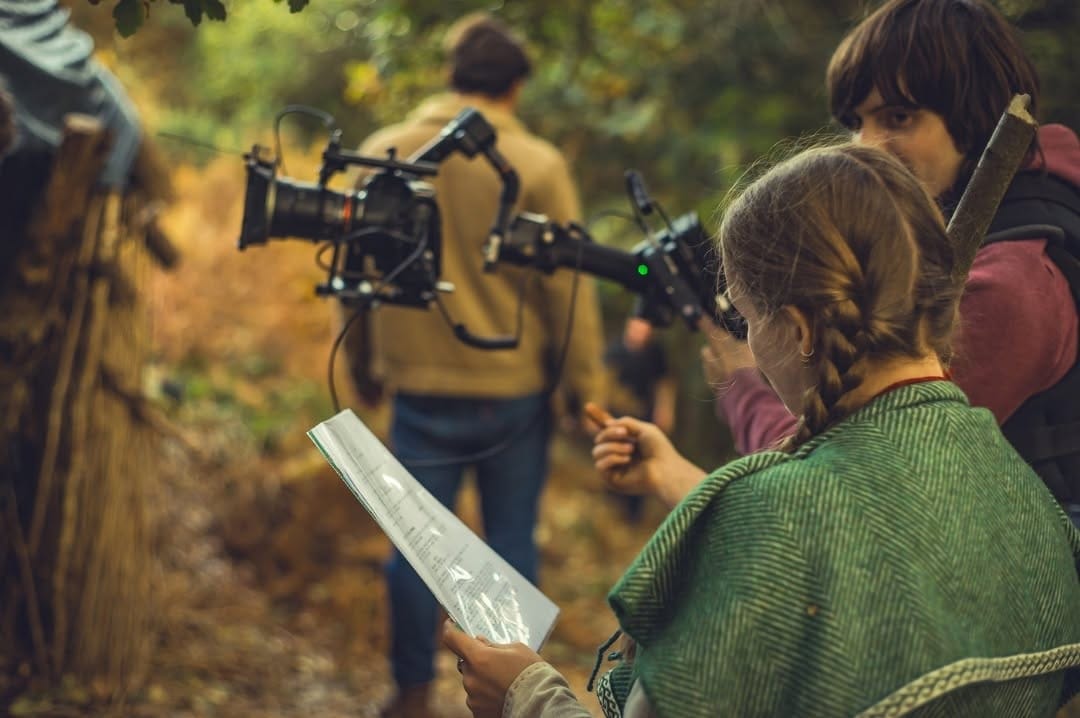 Filmmakers consulting a script and camera in a forest.