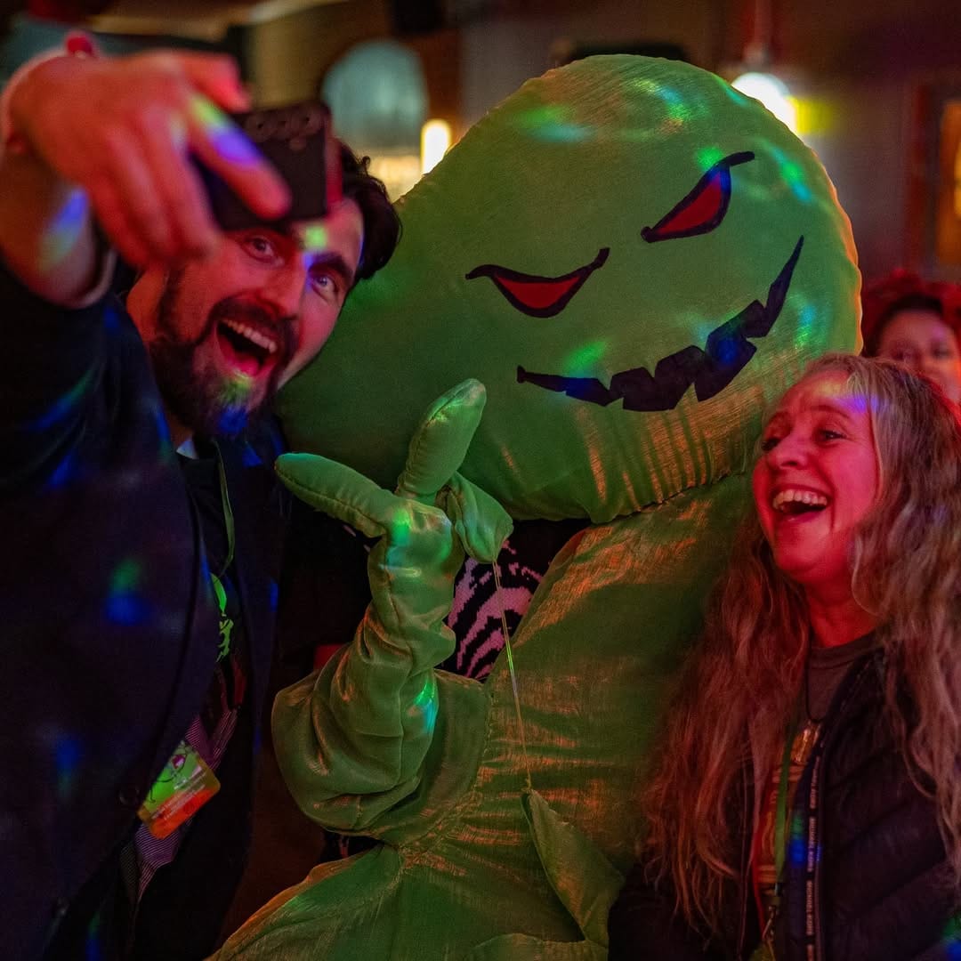 A green ghost mascot for the festival poses with two filmmakers.